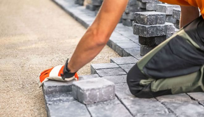 Worker laying gray paving stones beside a curb with a hand trowel