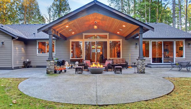 Modern house with a covered patio, outdoor seating, and a curved stone fire pit in front.