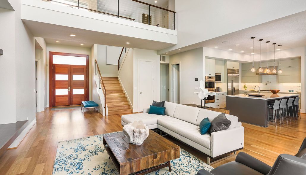 Bright open-concept living room with white sofa, wood staircase, kitchen, and dining area