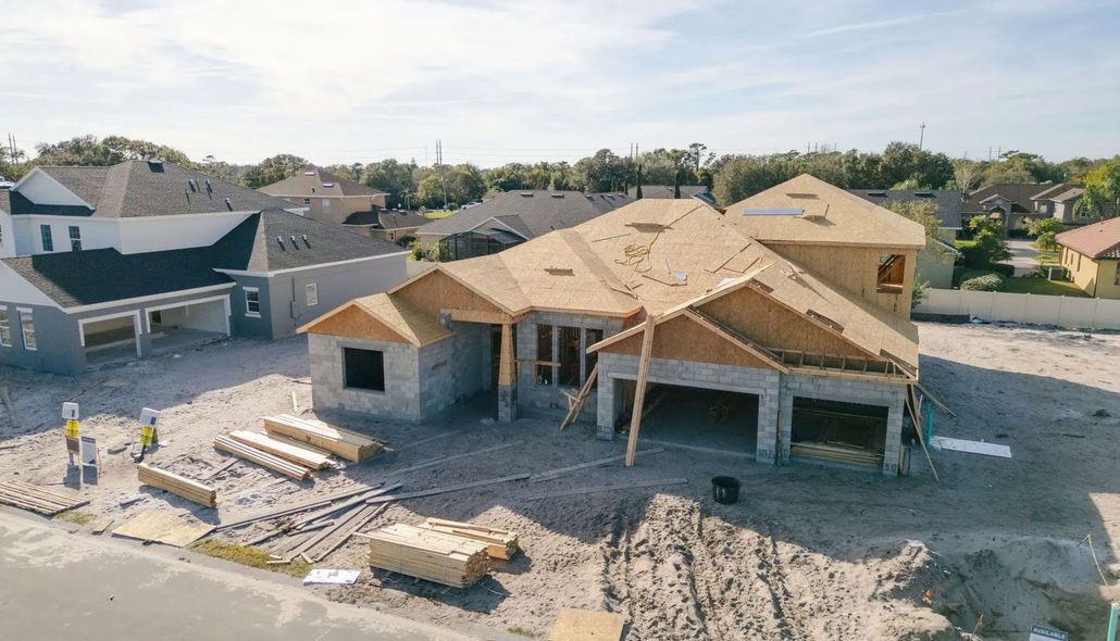 New suburban house under construction with roof trusses, exposed framing, and building materials scattered around