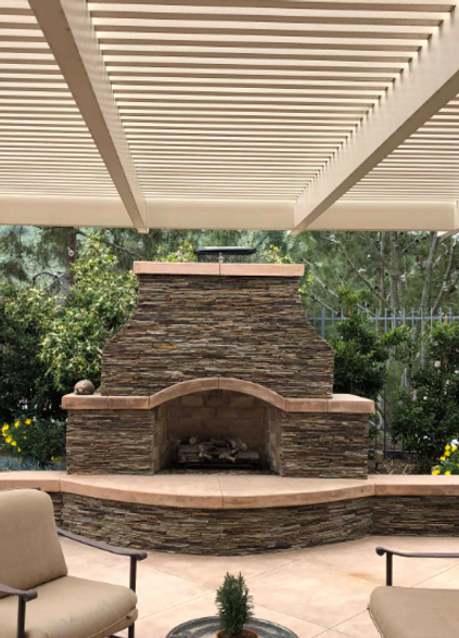 A stone fireplace is sitting under a pergola on a patio.