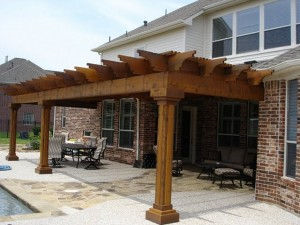 A wooden pergola is sitting on top of a patio next to a brick house.