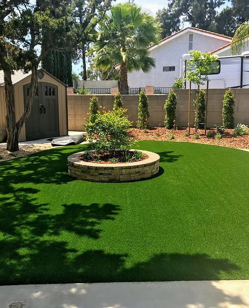 A backyard with a lush green lawn and a stone planter in the middle.