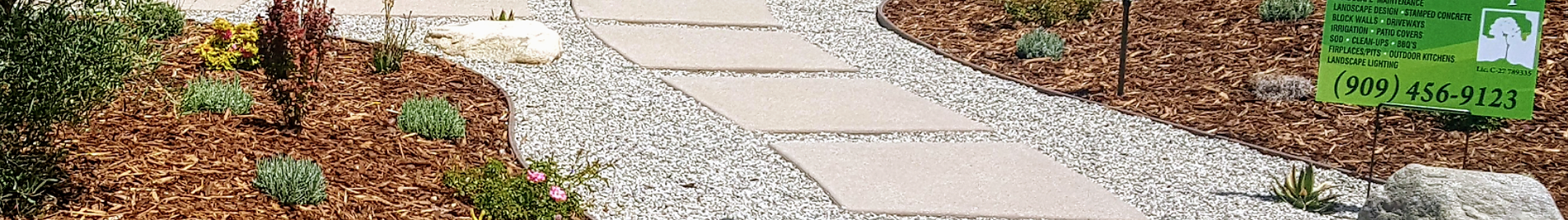 A blurred image of a stone walkway surrounded by mulch and trees.