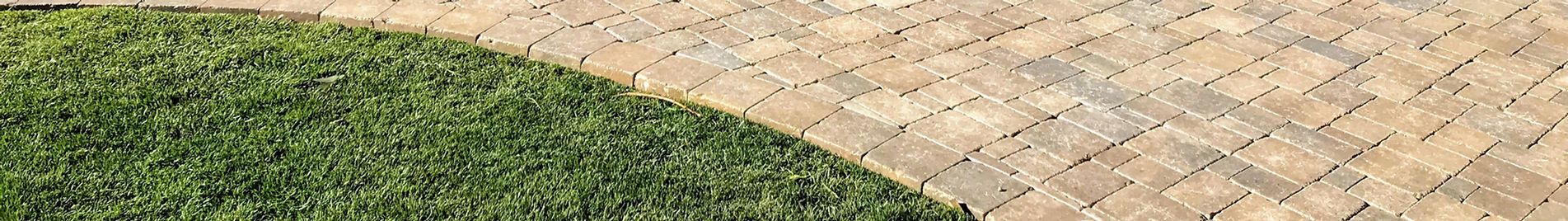 A close up of a brick walkway next to a lush green lawn.