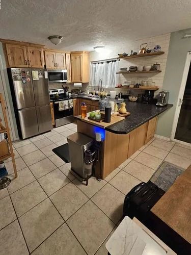 Kitchen with stainless steel appliances, wood cabinets, black countertop island, and tiled floor