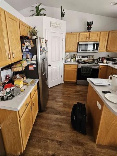 Bright kitchen with wood cabinets, stainless appliances, white door, and dark wood floor.