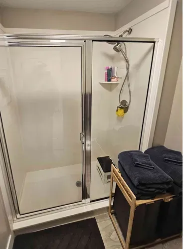 Bathroom shower with sliding glass doors, handheld showerhead, and folded towels on a stool