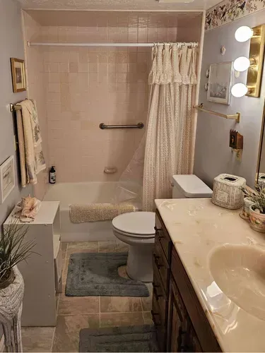 Small bathroom with a tub shower, toilet, vanity sink, and blue rug, viewed from the doorway