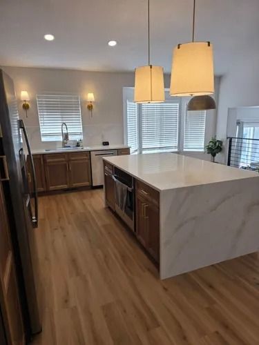 Bright modern kitchen with marble island, wood floors, pendant lights, and large windows