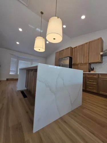 Modern kitchen with wood cabinets, white island, pendant lights, and hardwood floors