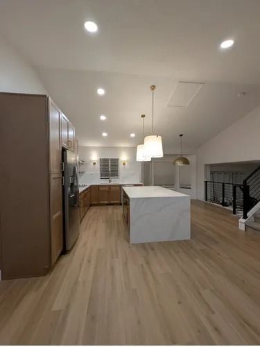 Modern kitchen with white island, wood cabinets, pendant lights, and light wood flooring