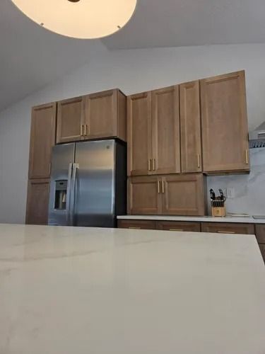 Modern kitchen with stainless steel refrigerator, wooden cabinets, and a white countertop