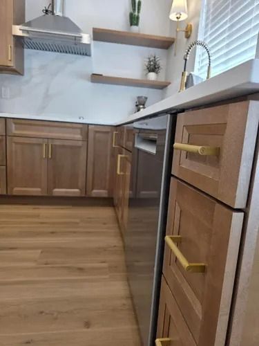 Modern kitchen with wood cabinets, light countertop, and black dishwasher beneath a window.