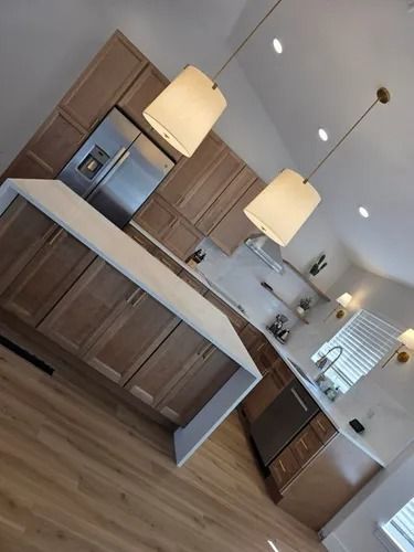 Modern kitchen with dark wood cabinets, white island, pendant lights, and stainless steel appliances.