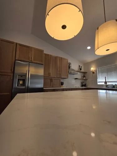Modern kitchen with wooden cabinets, stainless steel appliances, and pendant lights over a white countertop