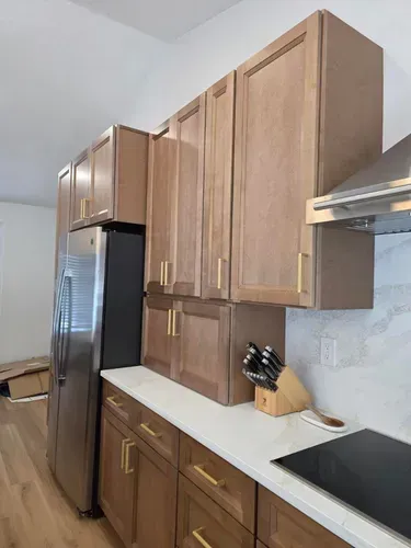 Kitchen with light wood cabinets, stainless steel fridge, white countertops, and black cooktop.