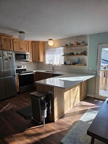 Bright kitchen with island, stainless steel appliances, wood cabinets, and a sunlit window.