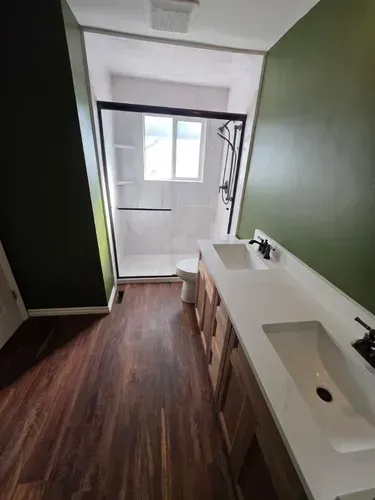 Narrow hallway with dark wood floor, green walls, and a white sink counter near a bright doorway.