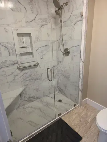 Modern shower with glass doors, marble-look tile, built-in niche, handheld showerhead, and dark floor threshold