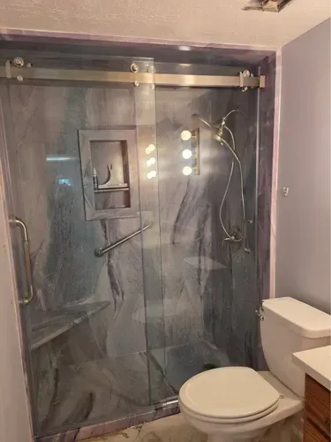Small bathroom with a glass shower stall, toilet, vanity mirror lights, and gray walls.