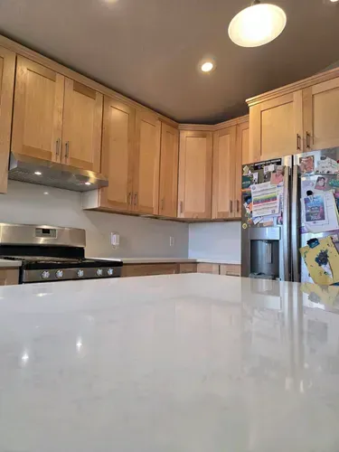 Bright kitchen with light wood cabinets, white countertop, stainless stove, and a refrigerator covered in magnets and notes