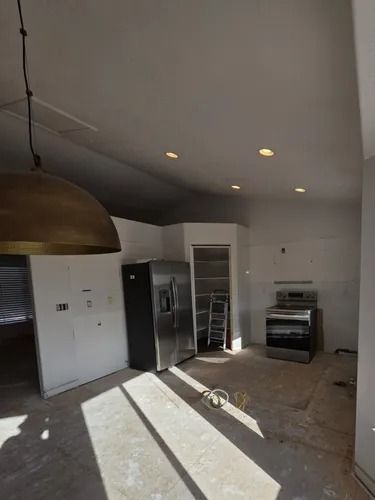 Modern kitchen under construction with white cabinets, stainless appliances, and sunlight on the floor