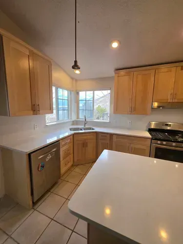 Bright kitchen with wooden cabinets, white countertops, tiled floor, and a central island.
