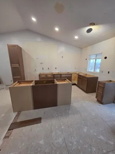 Unfinished kitchen with bare cabinets, white walls, and a window letting in daylight.