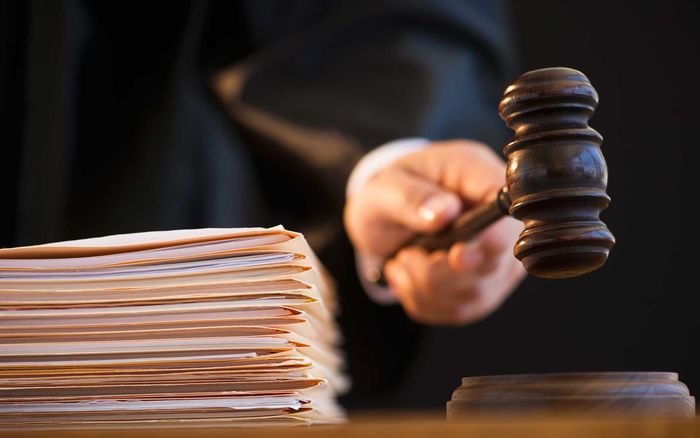 A judge is holding a wooden gavel in front of a stack of papers.