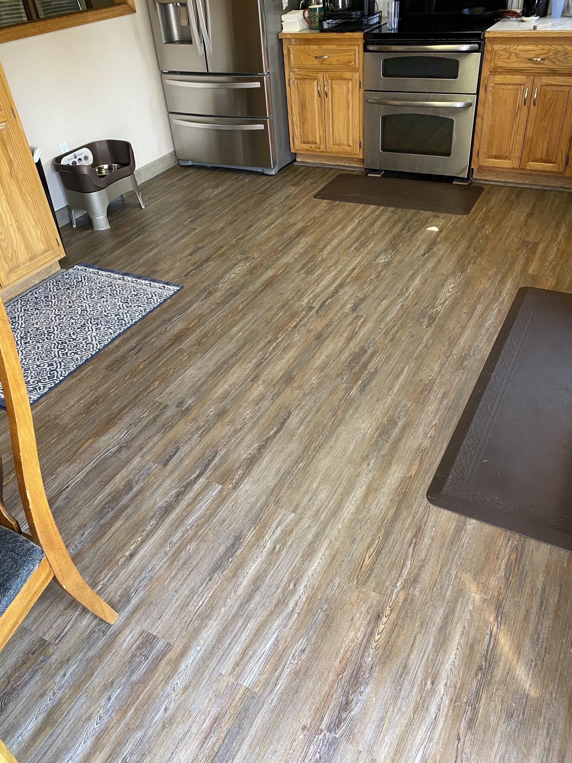 A kitchen with a wooden floor , stainless steel appliances , a refrigerator and a stove.