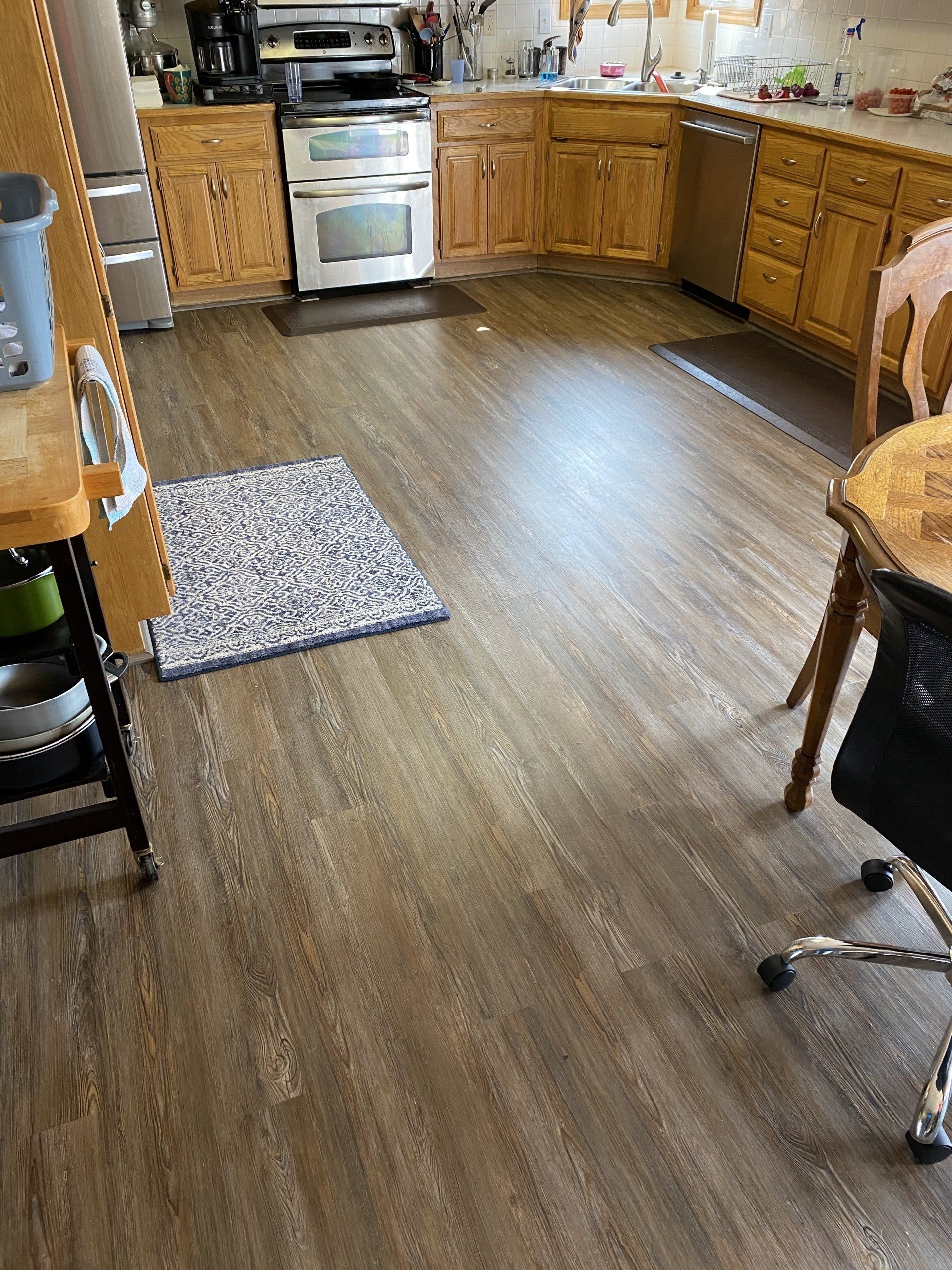 A kitchen with hardwood floors , wooden cabinets , a stove and a chair.