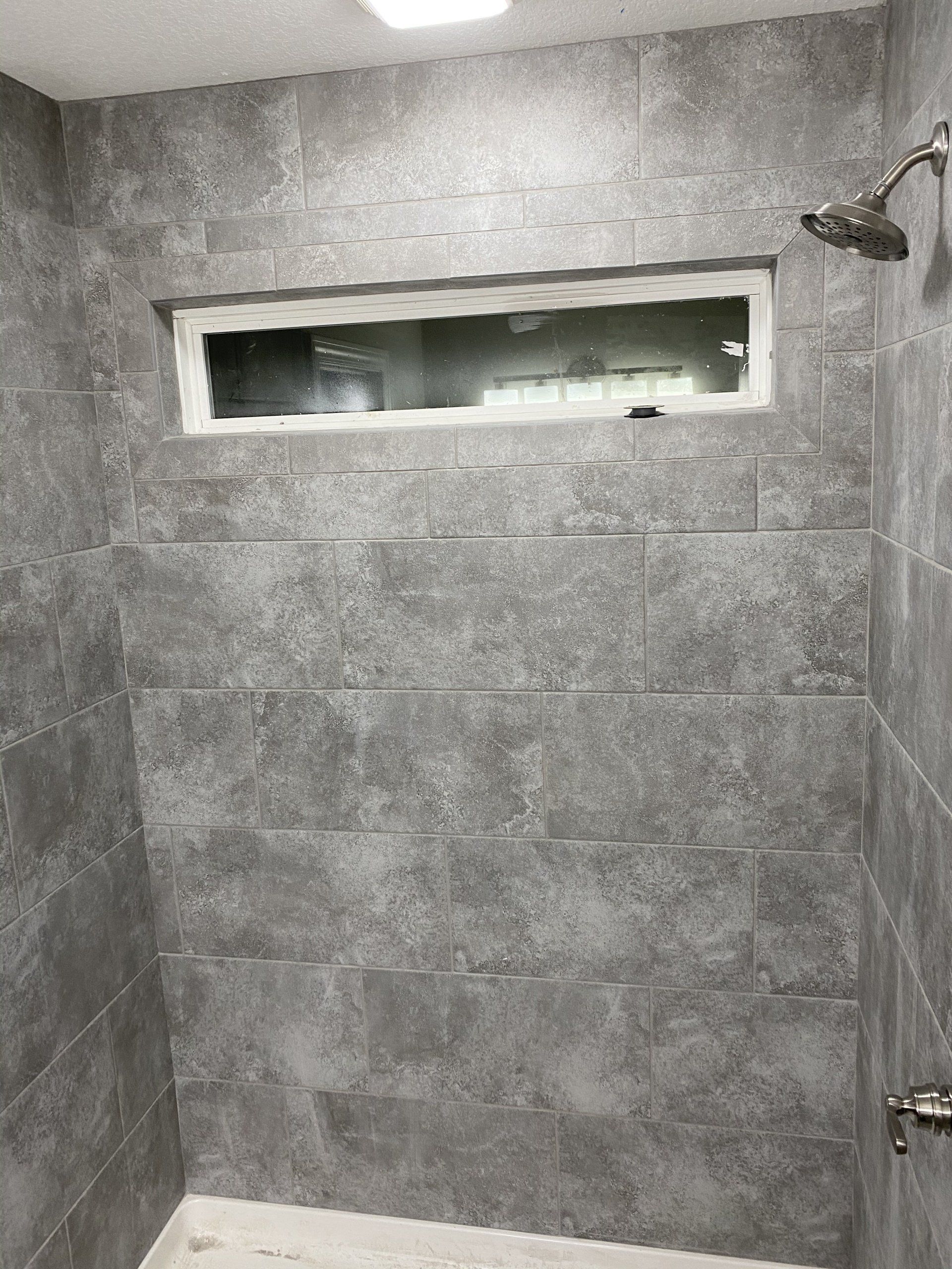A shower with gray tiles and a window.