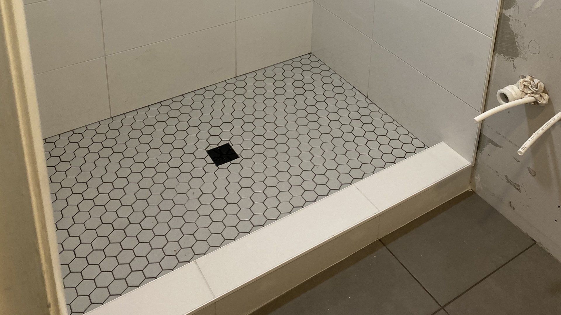 A shower stall with a hexagonal tile floor in a bathroom.