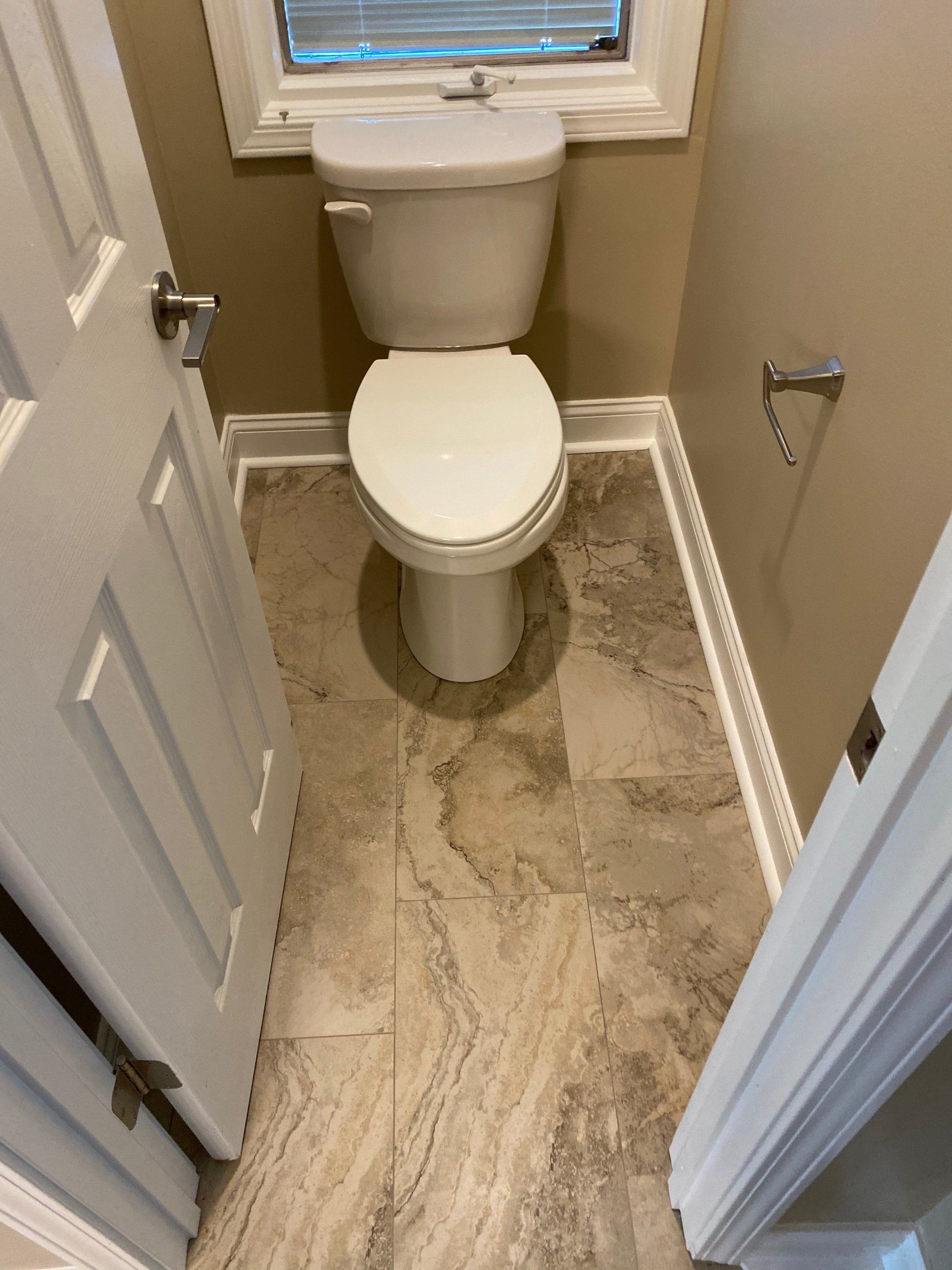A toilet is sitting in a small bathroom next to a window.
