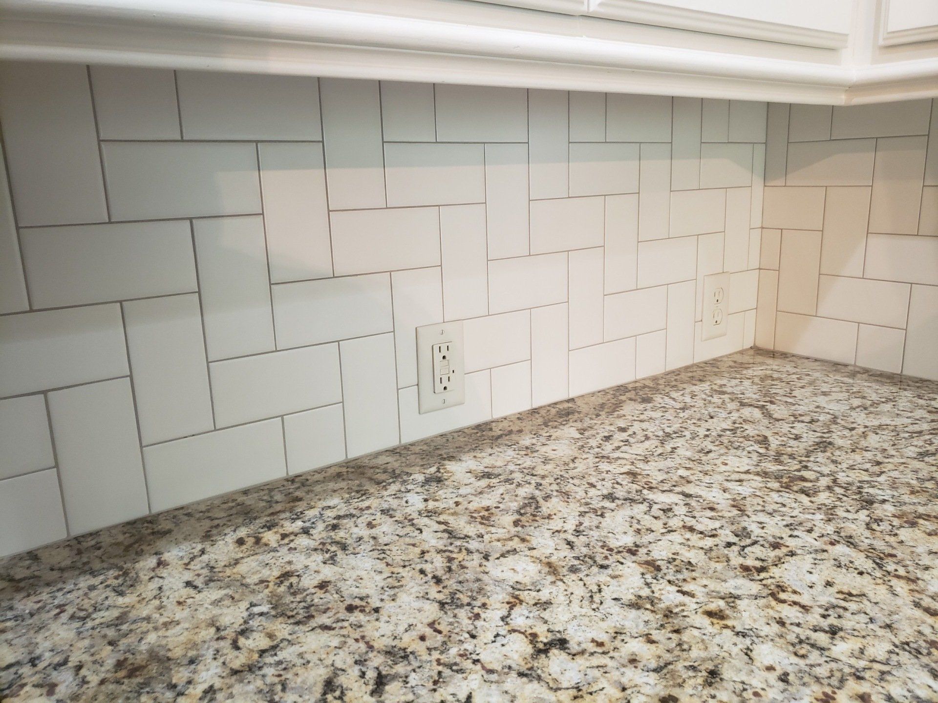 A kitchen counter with white tiles and granite counter tops.