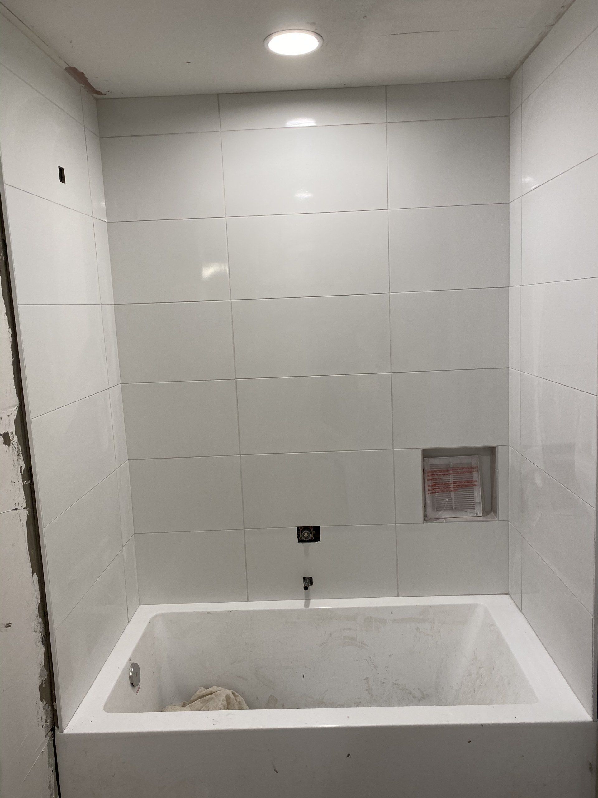 A bathtub in a bathroom with white tiles on the wall.