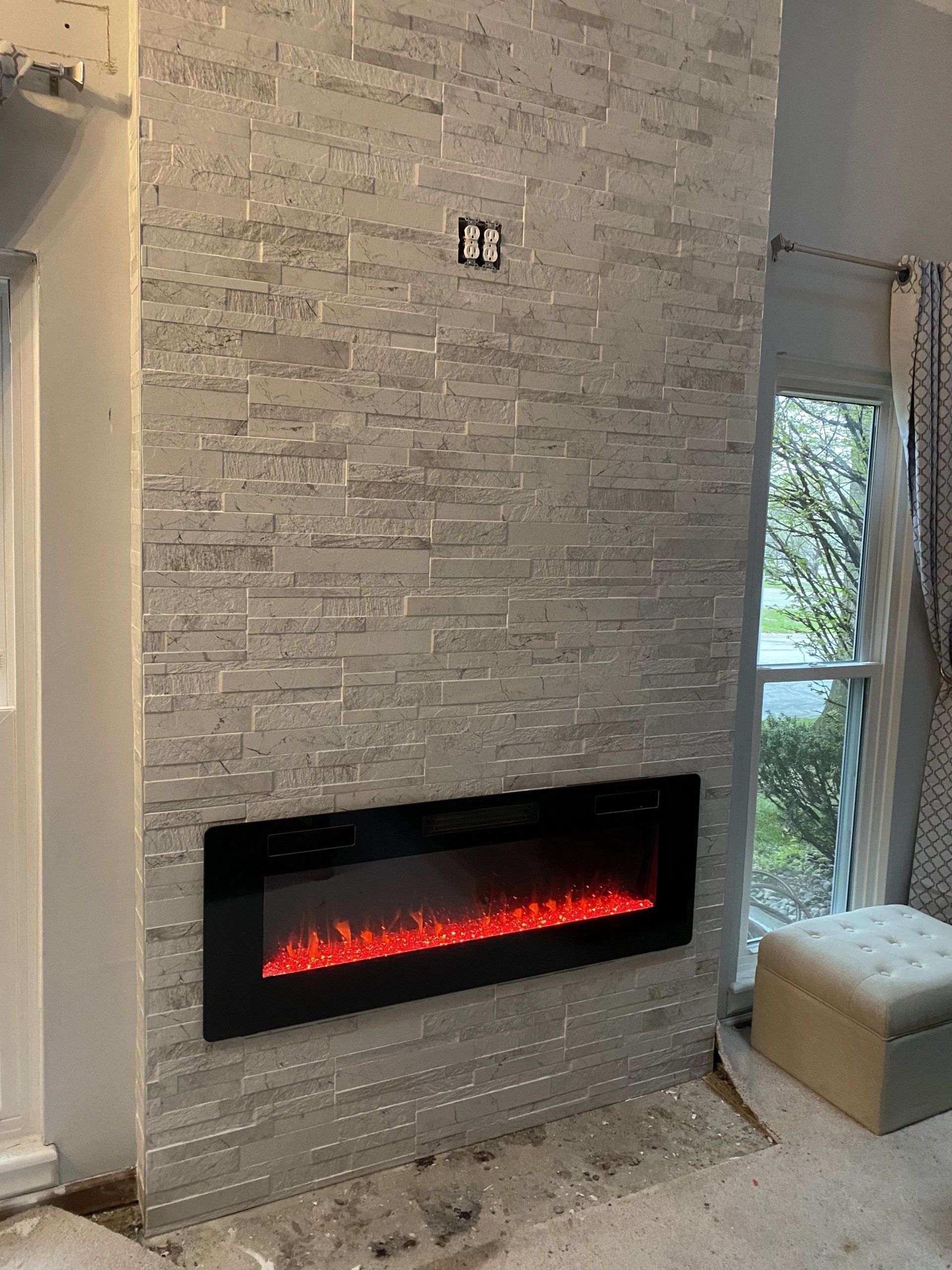A fireplace is being installed in a living room next to a window.