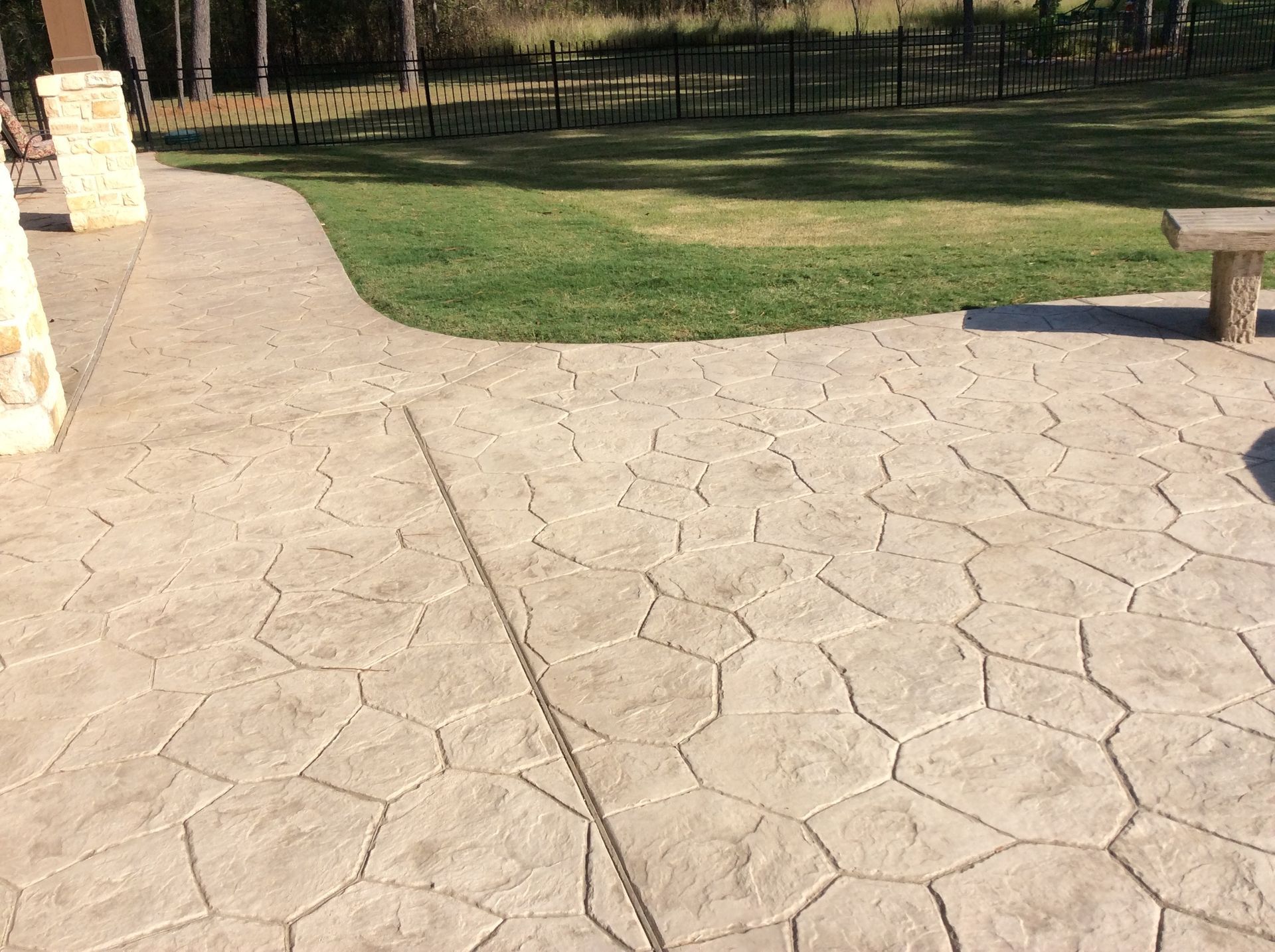 A concrete patio with a bench and a fence in the background.