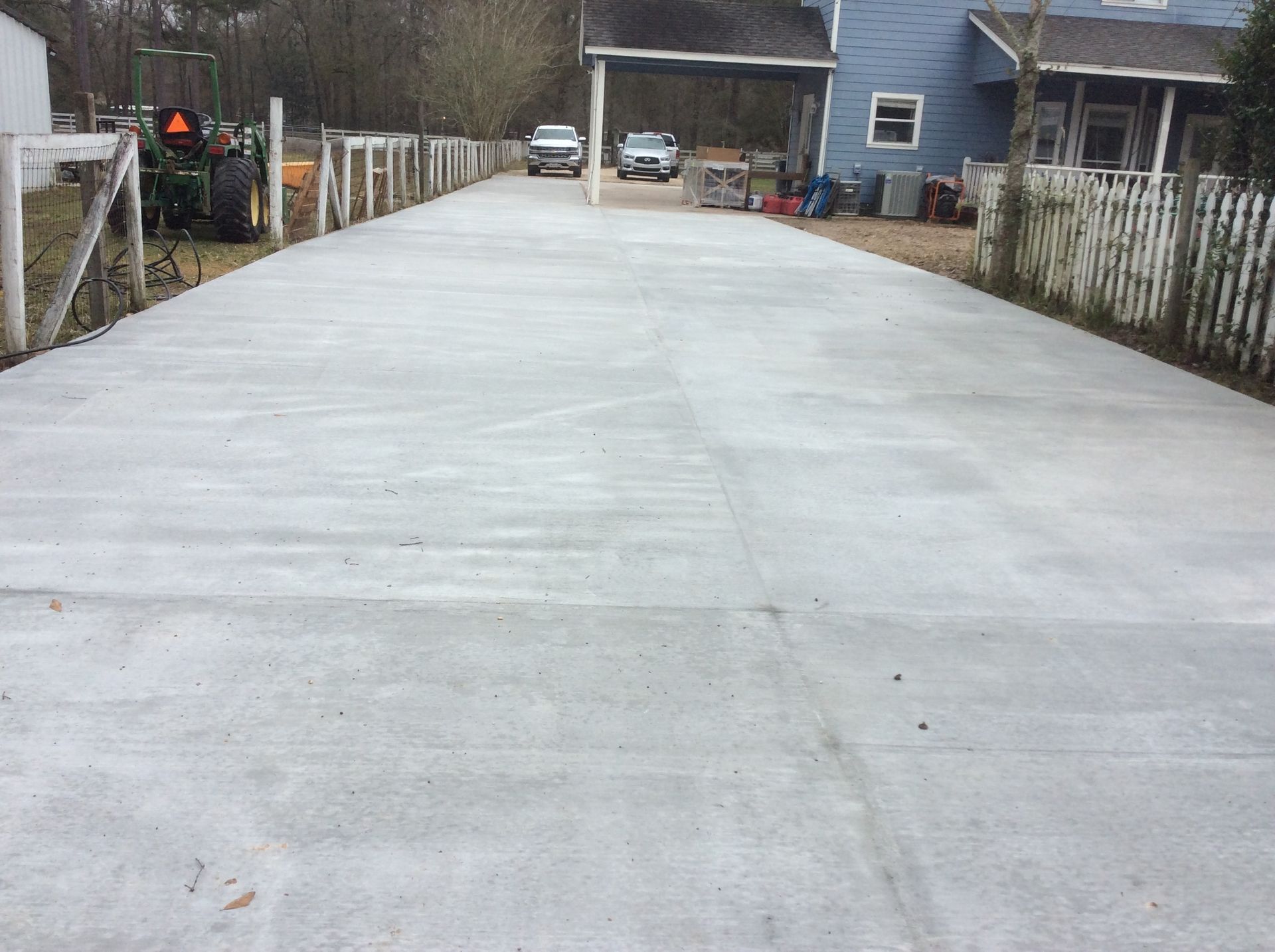 A tractor is parked on the side of a concrete driveway leading to a house.