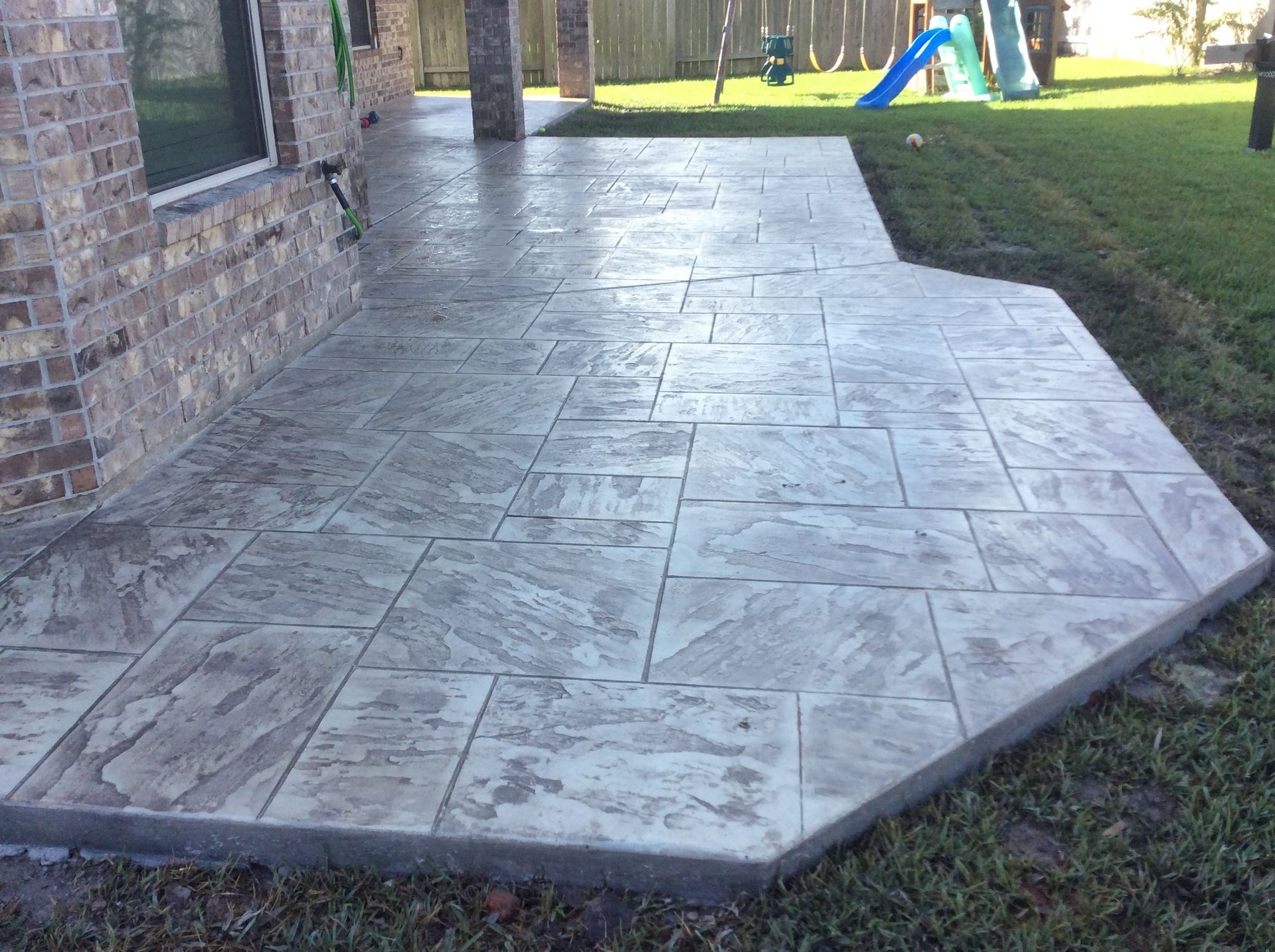 A concrete patio in a backyard with a playground in the background.