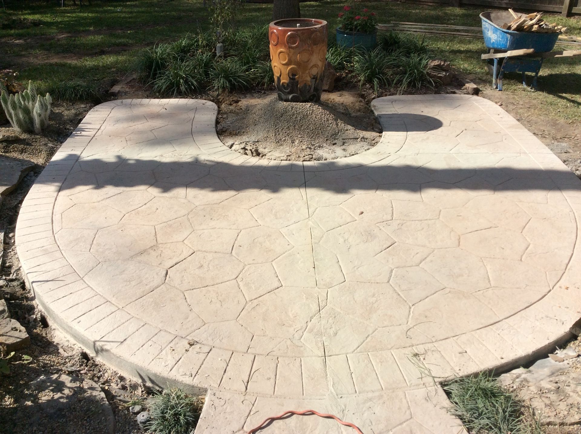 A concrete patio with a wheelbarrow in the background and a potted plant in the middle.