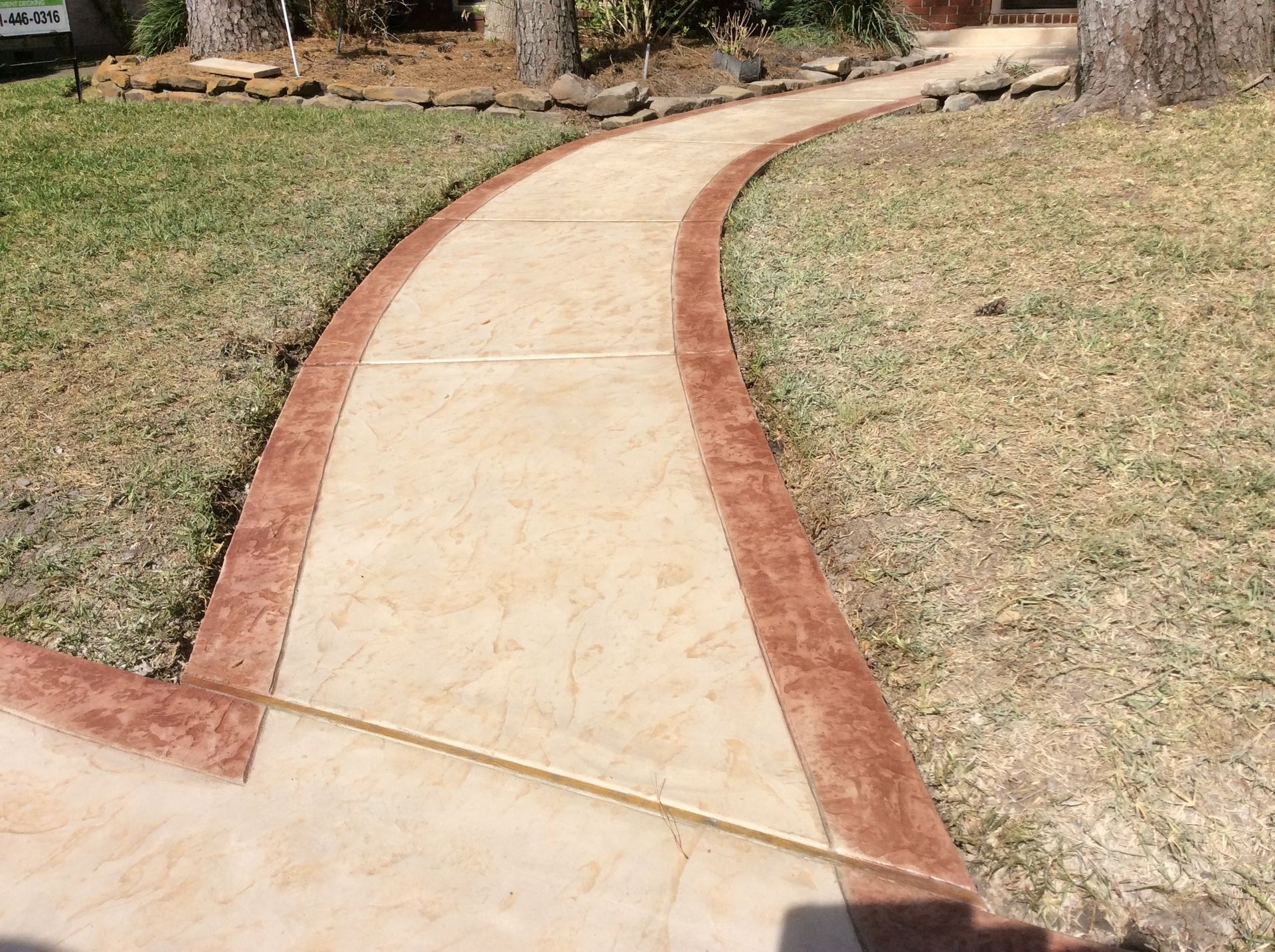 A concrete walkway with a red border is going through a grassy area.