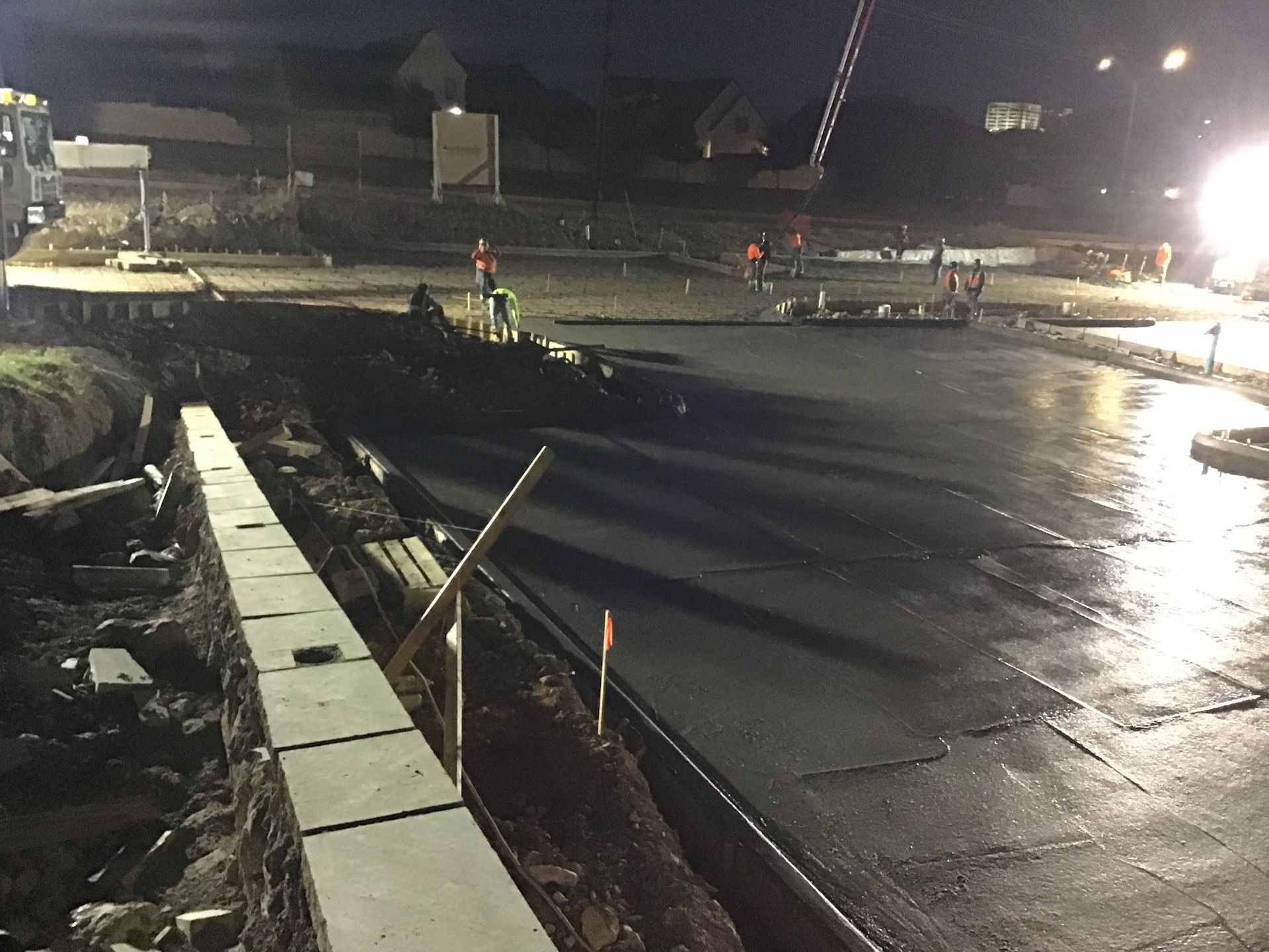 Construction site at night, pouring concrete for a road. Workers and equipment visible.