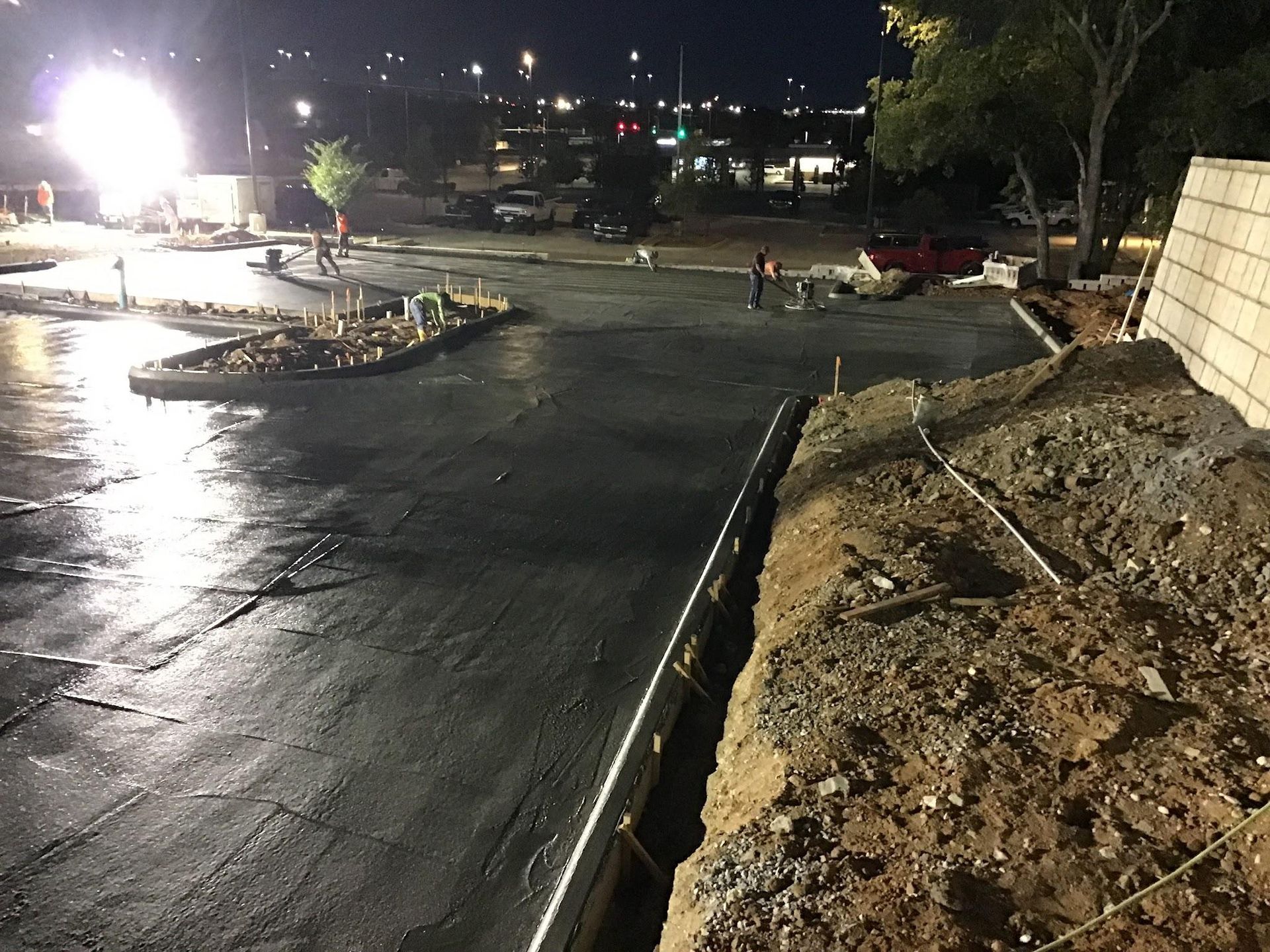 Construction site at night with workers, wet concrete, and bright lights.