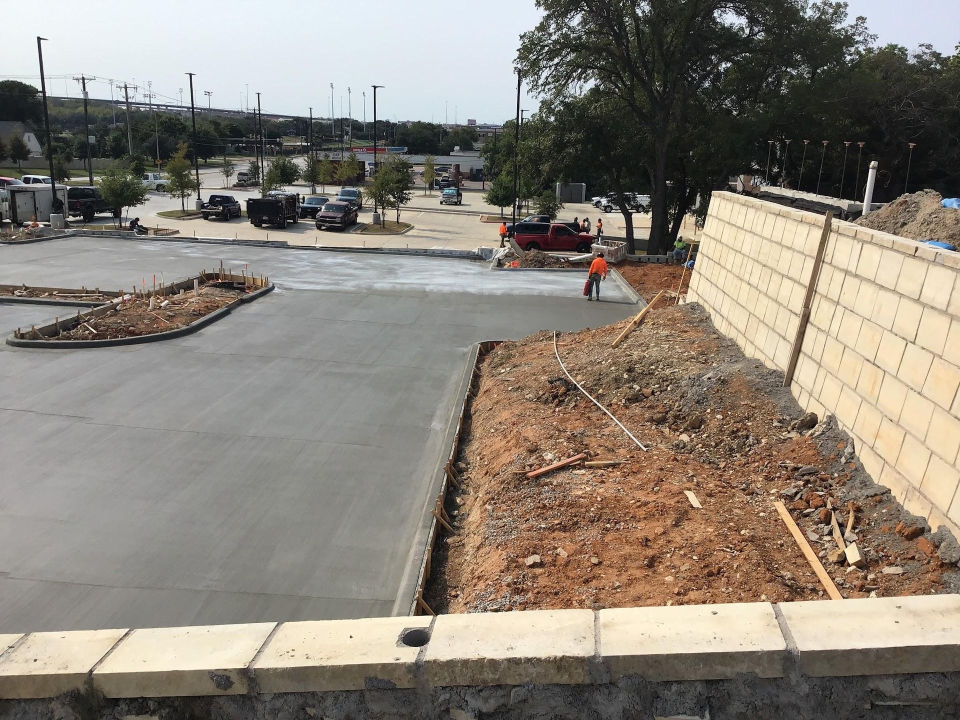 Concrete being poured in a parking lot under construction; worker in orange vest.