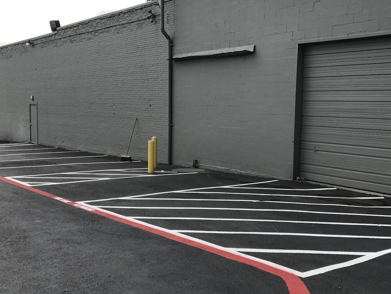 Gray building exterior with parking lot; white lines define spaces, red borders.