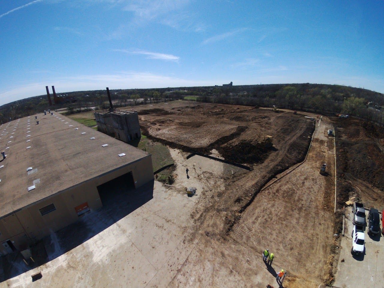 Construction site with cleared land, building, and vehicles under a blue sky.