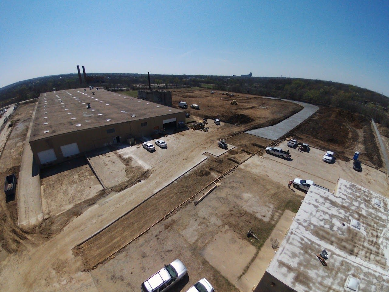 Aerial view of a large industrial building with a flat roof, surrounded by construction and parked vehicles.