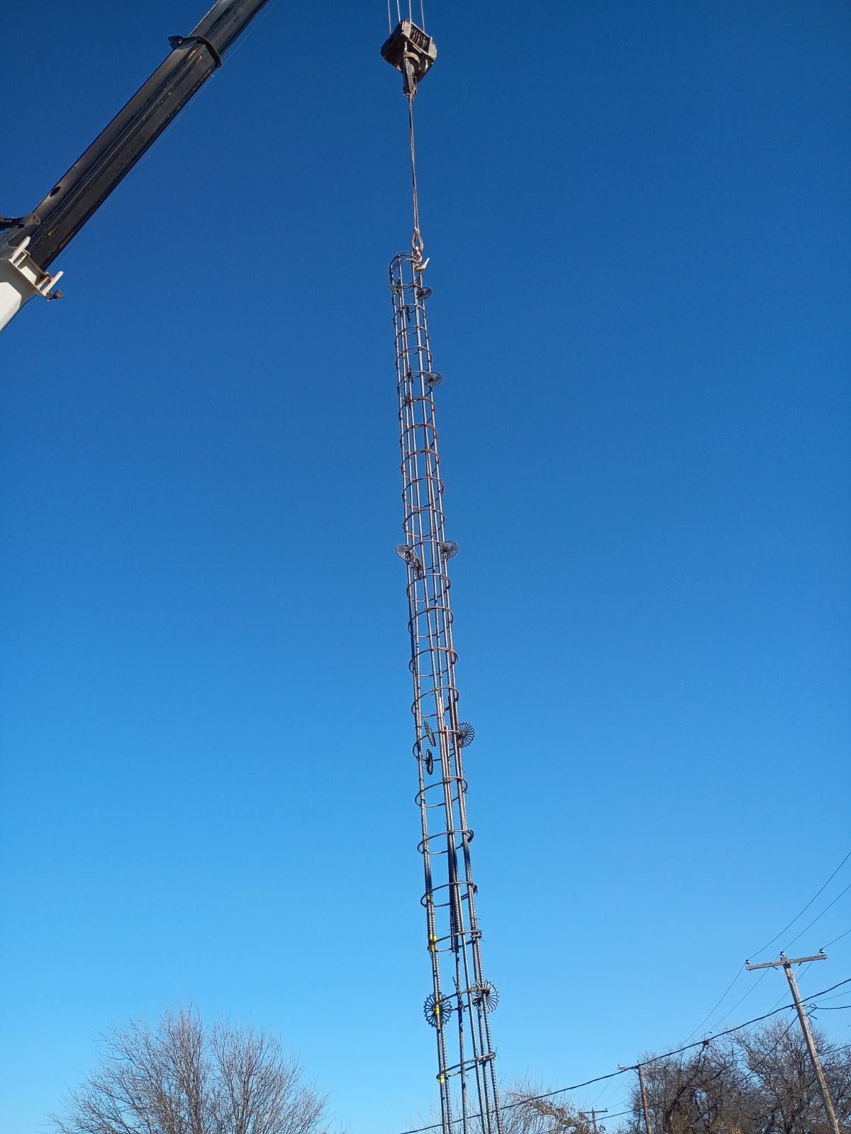 Crane lifting a tall metal lattice structure against a clear blue sky